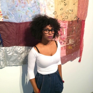 Image of Artis T.J. Dedeaux-Norris leaning against one of her paintings